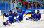 a group of Para ice hockey players raise their arms in celebration on the ice