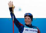 a female Nordic skier smiles and waves 