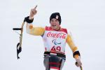 a male Para alpine skier raises his arm in celebration