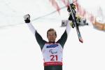 a male skier raises his arms in celebration holding his skies