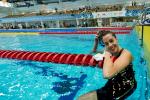 a female Para swimmer smiles in the water as she removes her swimming cap