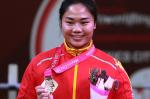 female powerlifter Yujiao Tan holds up her gold medal and smiles