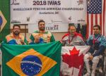 four male wheelchair fencers on the podium including Jovane Guissone holding a Brazilian flag