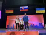 three shooting Para sport athletes with Veronika Vadovicova in a wheelchair in the centre, on a podium with the German, Slovakian and Ukrainian flags hanging behind them