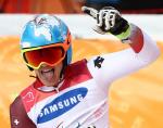 male Para alpine skiing Theo Gmur punches the air and smiles after crossing the finish line