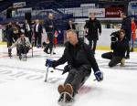 A group of people on an ice rink with a man trying Para ice hockey