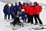a group of skiing technical people standing behind a male Para alpine sit skier on the ski slope