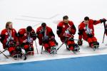 five Canadian Para ice hockey players sit looking sad on the ice holding silver medals