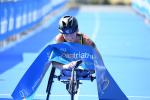 Australian woman in racing wheelchair crosses the finishline tape at a triathlon event