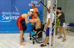 An female swimmer talking to a male swimmer in a wheelchair with four people in the background