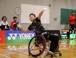 Korean male badminton player in wheelchair leans back to hit a birdie