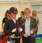 British female dressage athlete holds bucket of prize with an organiser