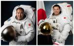 two male astronauts smiling in their space suits and standing beside the Japan flag