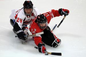 A picture of 2 men in a sledge playing ice hockey