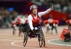 A picture of a woman in the wheelchair on a track celebrating with her hand up