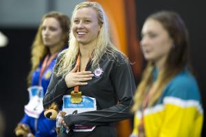Three women on a podium, one of them smiling, in focus and looking to the camera