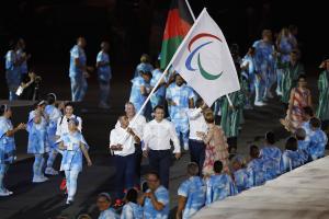 Group of people walking with a big flag showing the Paralympic symbol
