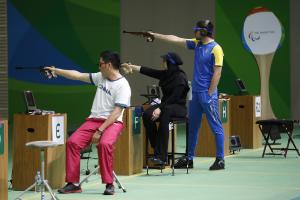 Two sitting and one standing shooting para athlete aiming at the targets
