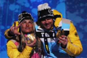 A picture of a woman showing her gold medal with a man during a medal ceremony