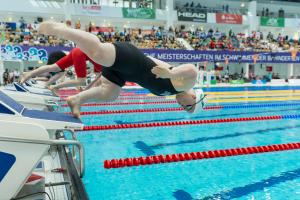 A short stature female swimmer jumping in the water in front of other swimmers